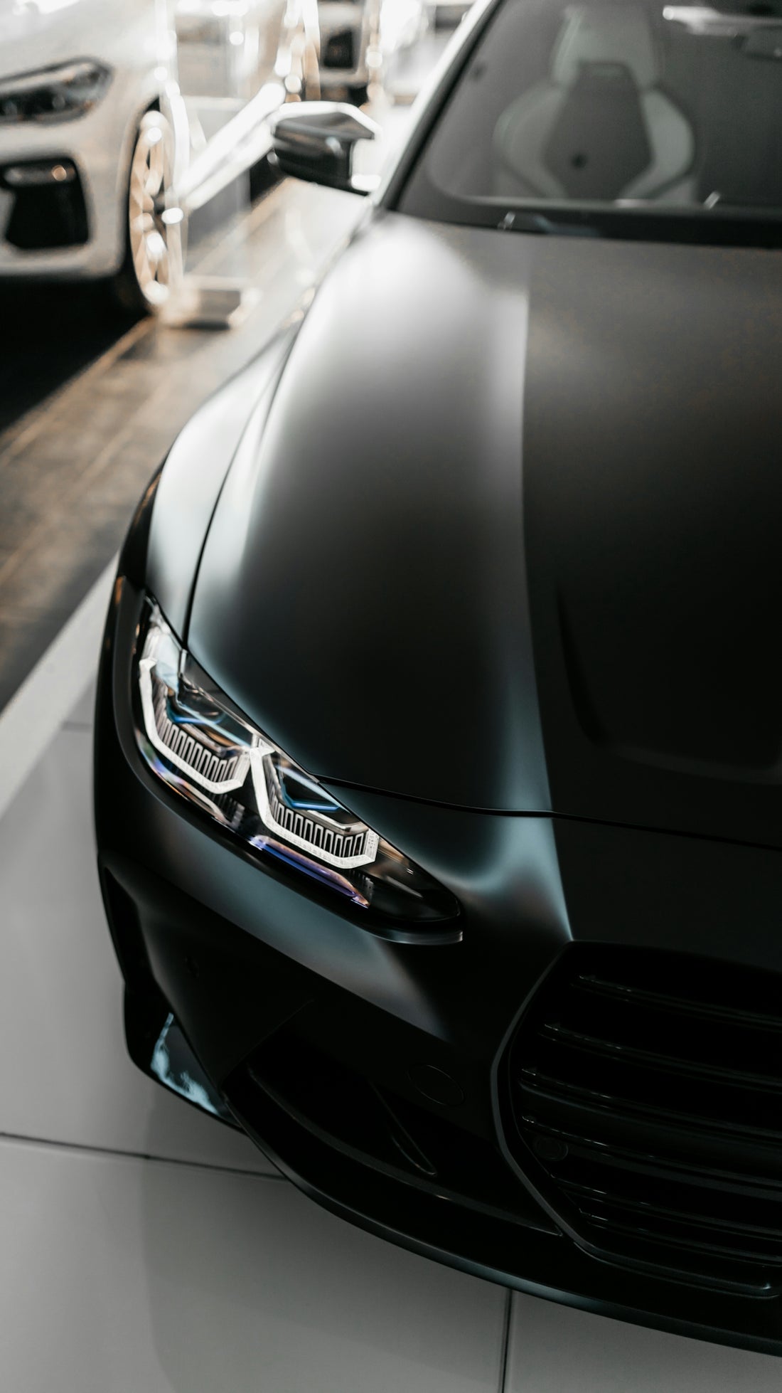 A matte black car with illuminated LED headlights in a showroom